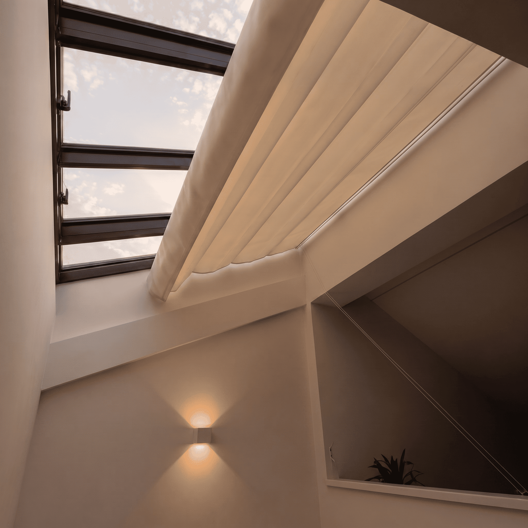 Lucernario interior con estructura oscura y toldo corredero de tela beige parcialmente extendido en una habitación de paredes blancas con luz cálida.