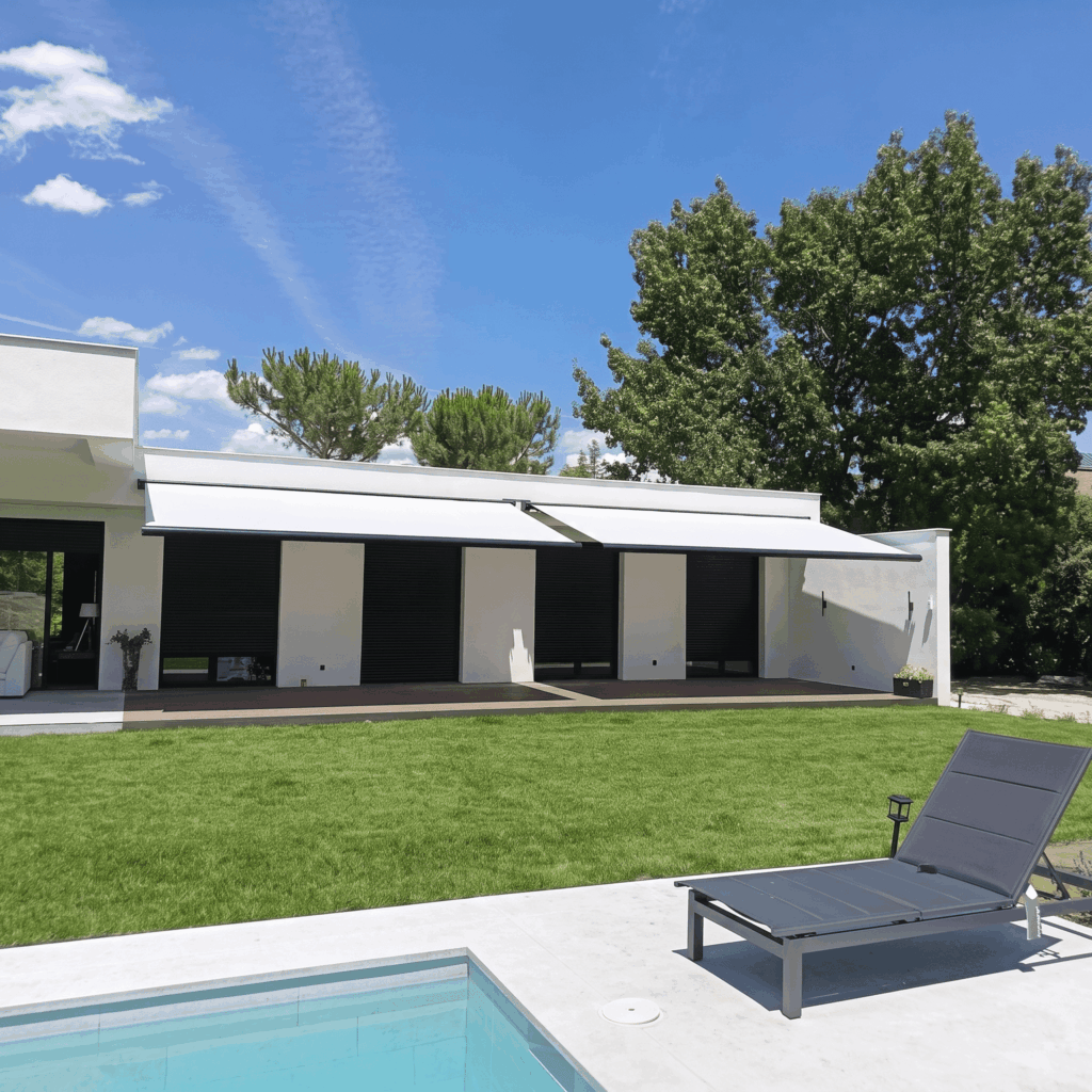 Fachada de casa moderna blanca con grandes ventanales, persianas negras, dos toldos extendidos y una piscina con tumbona.
